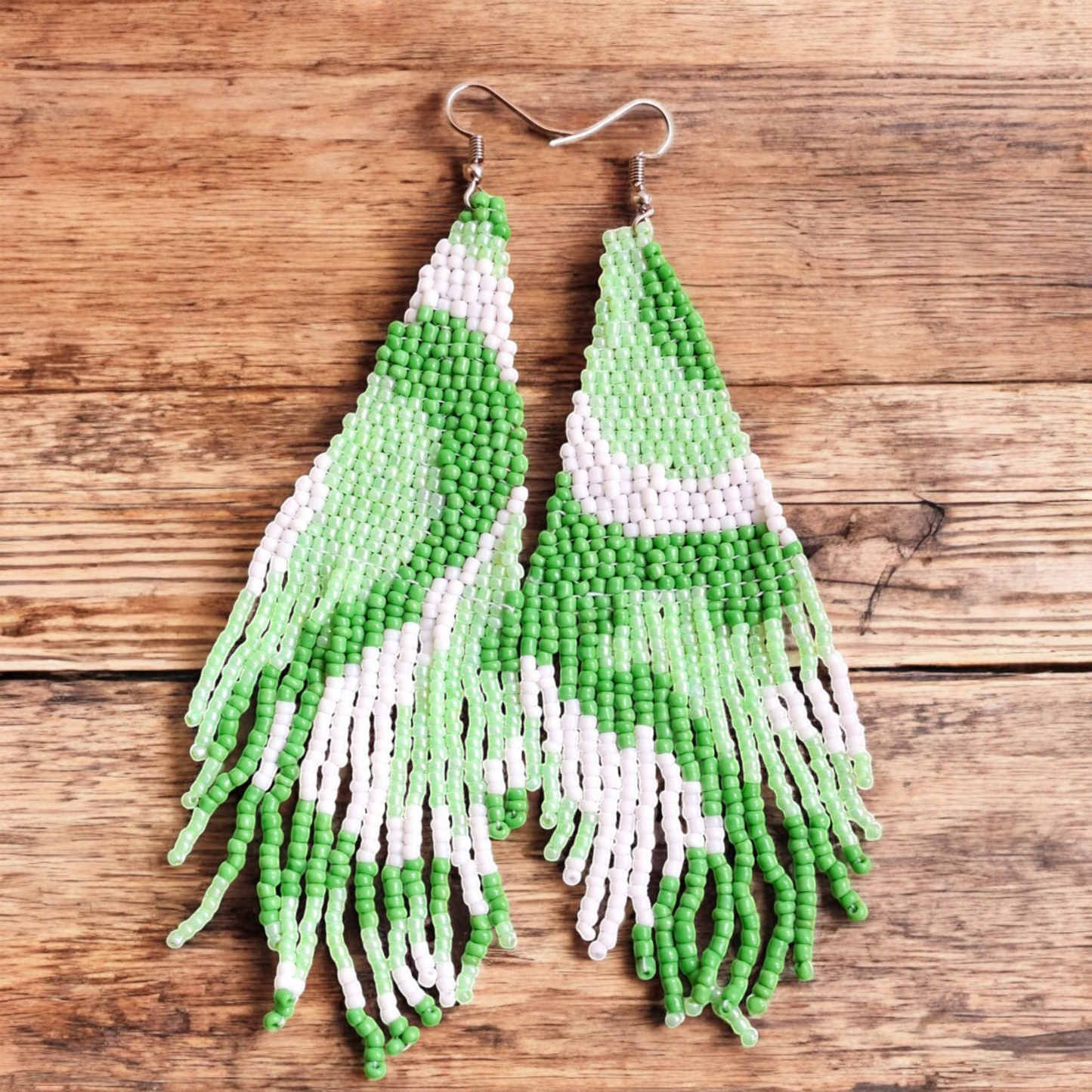 Handmade Waves Cascade earring in Mint Green with hints of white and grass green in a waterfall-inspired design on a wooden backdrop.