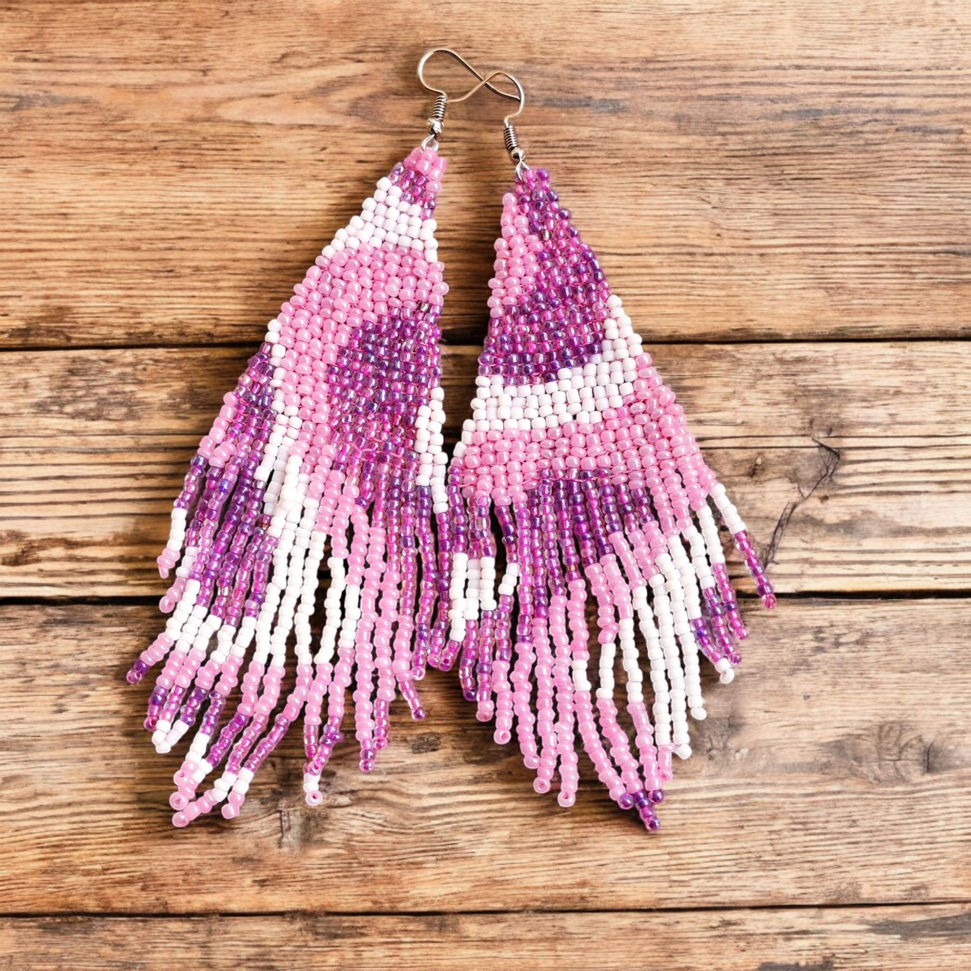 Handmade Waves Cascade earring in Lilly Pilly Pink with accents of white and purple in a waterfall-inspired design on a wooden backdrop.